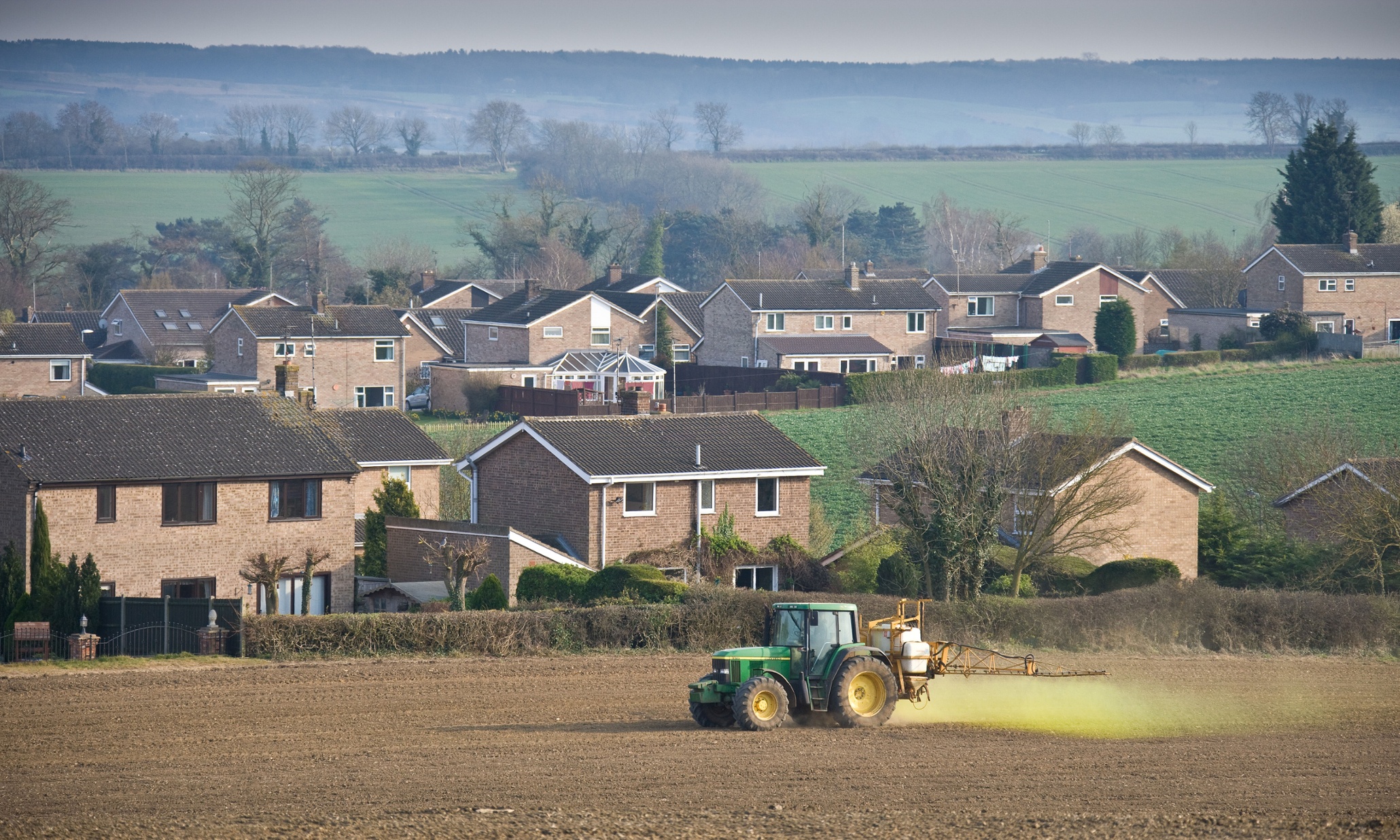 A crop sprayer applying pesticide close to residential housing